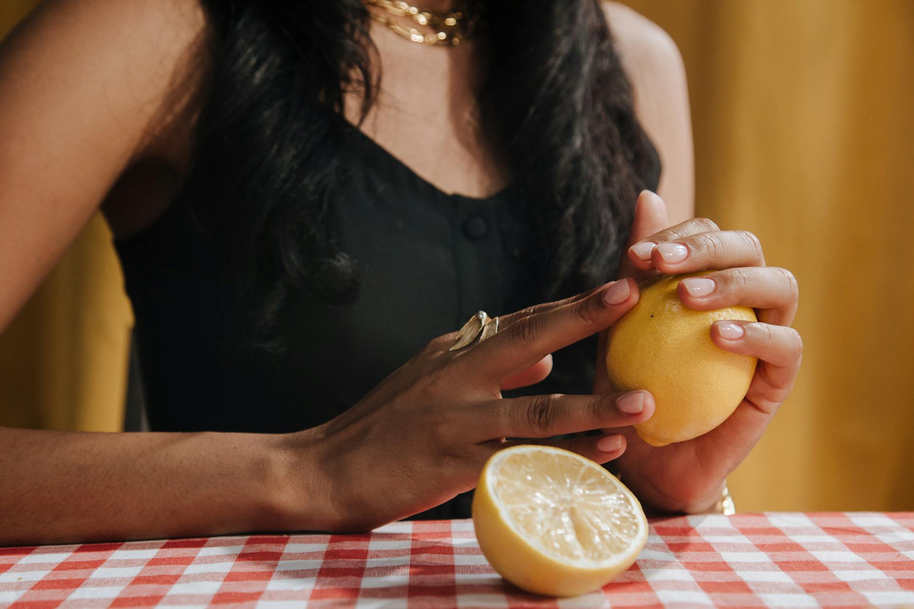 Una donna con i capelli neri tiene un limone fresco mentre è seduta a un tavolo da pranzo.