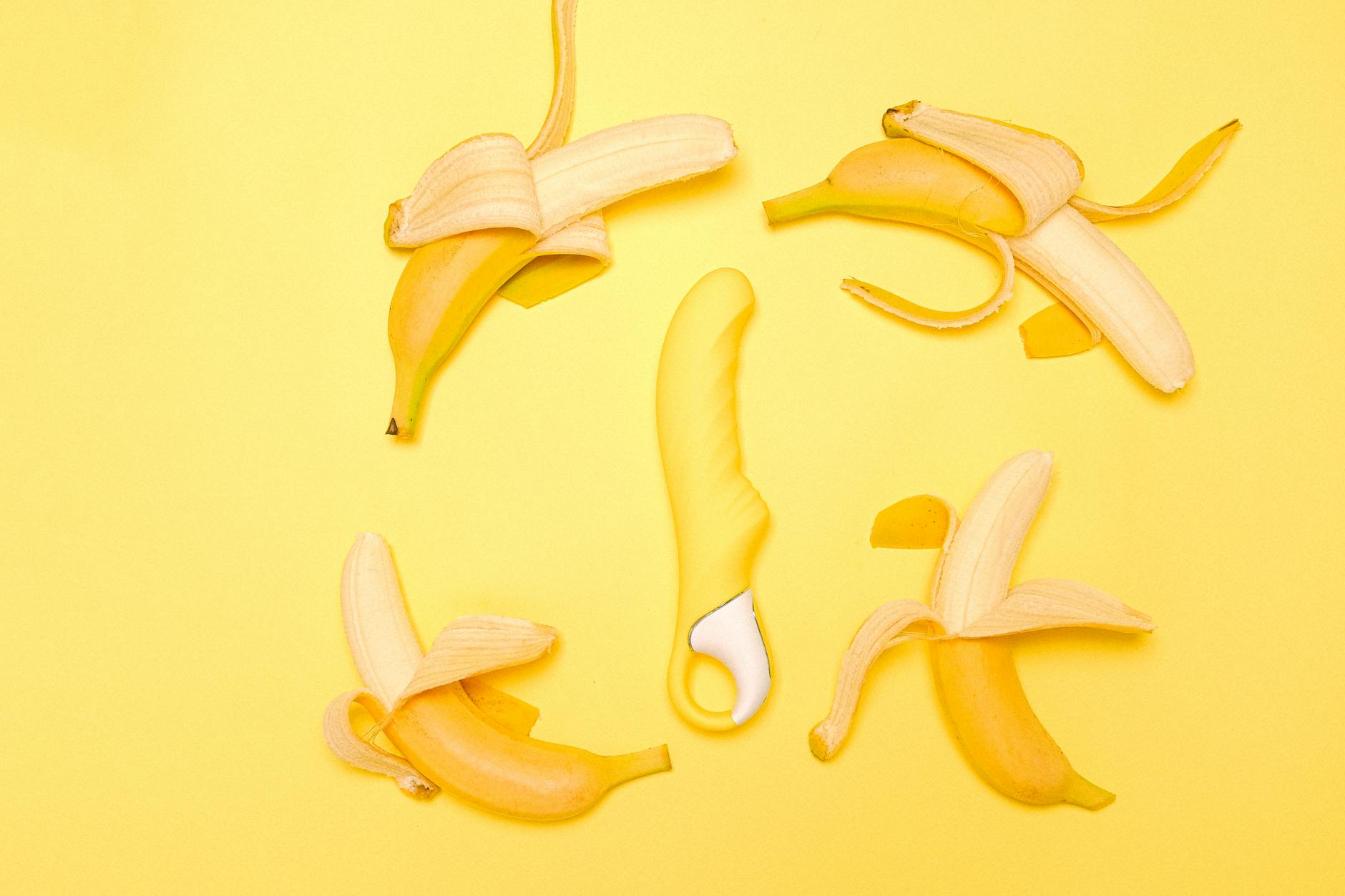 A bright yellow lemon vibrator on a yellow background surrounded by fresh lemons