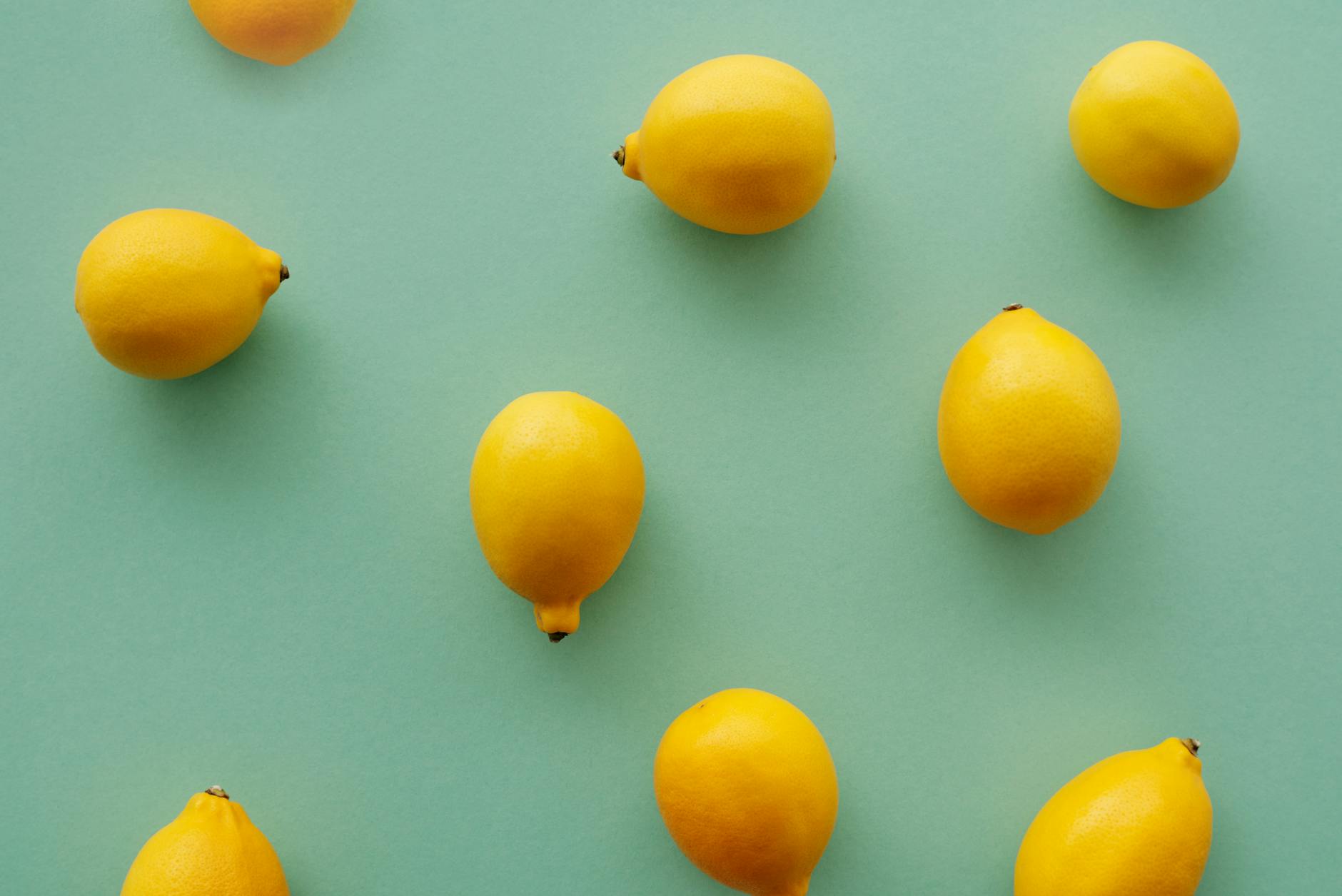 Limoni gialli brillanti disposti su uno sfondo verde pastello, in una composizione di flat lay fresca e vibrante
