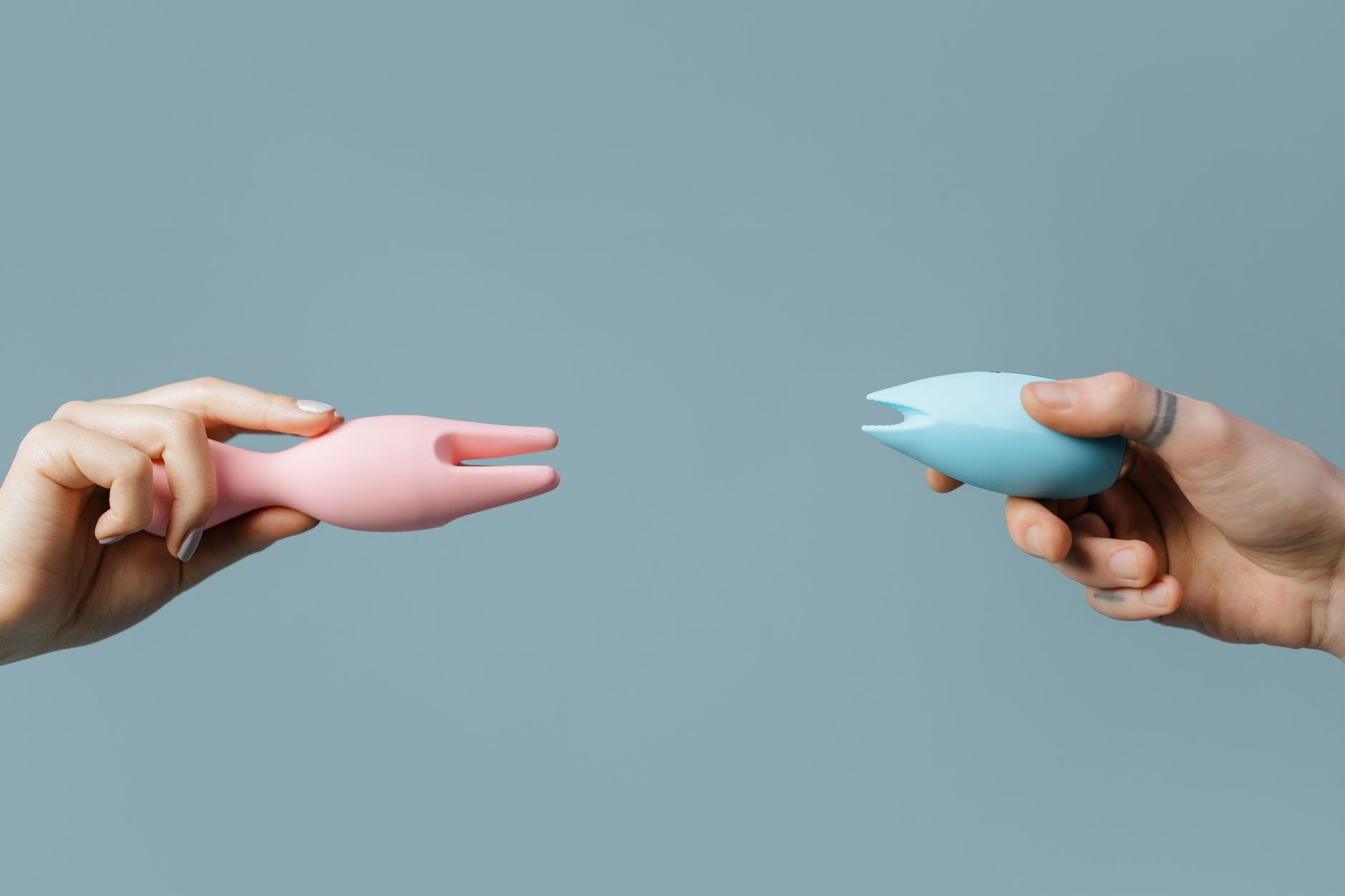 Donna con occhiali che tiene in mano vibratori in silicone blu e rosa in atteggiamento contemplativo