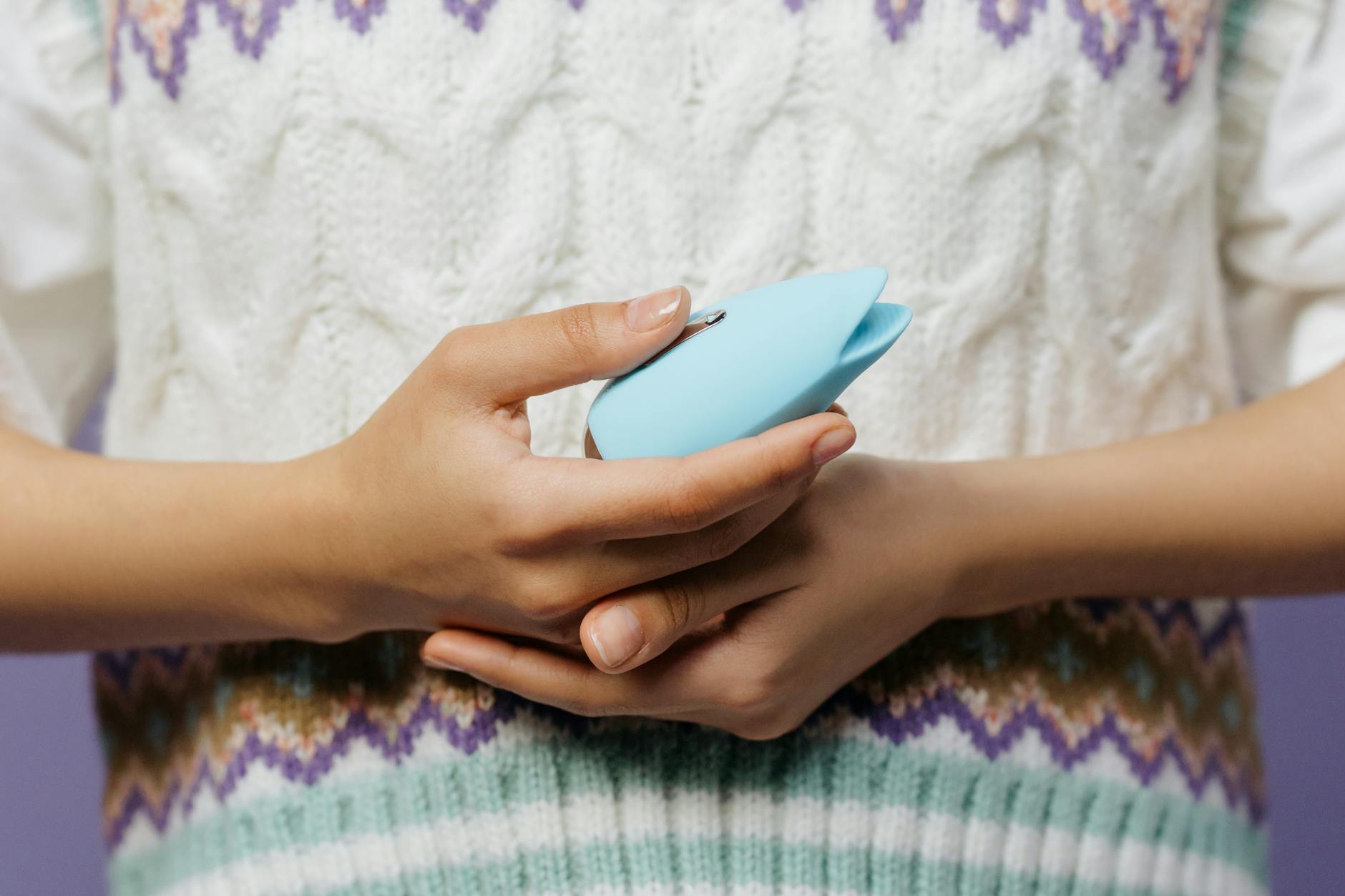 Mani che tengono un massaggiatore personale blu su un maglione lavorato a maglia